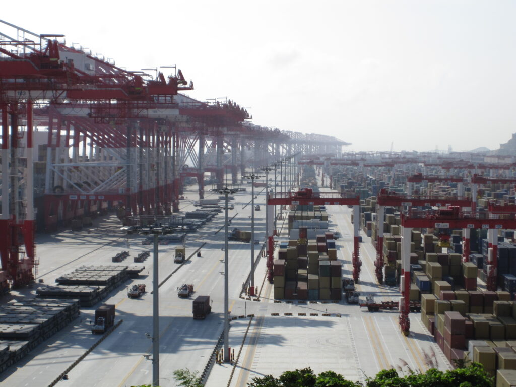 Rows of shipping containers and red gantry cranes at Yangshan Deepwater Port in Shanghai.