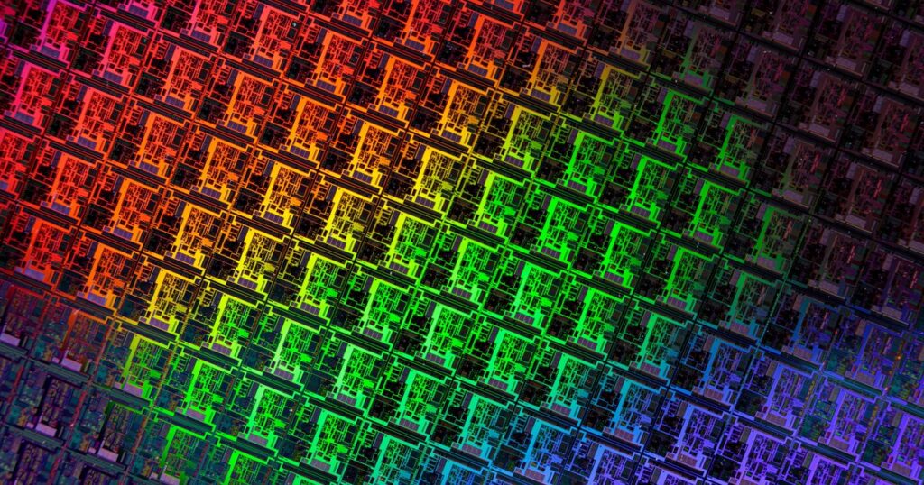 Close-up of a silicon wafer patterned with chip dies, lit in rainbow colours